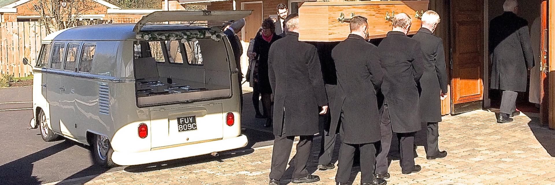 People removing and carrying a coffin from a VW splitscreen campervan