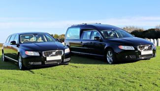 Hearse and other vehicle parked side by side on grass with blue sky background
