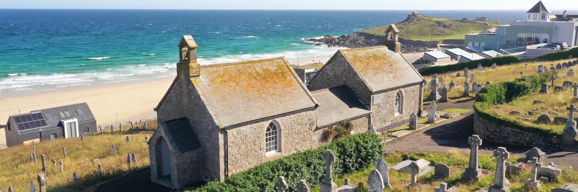 A view from up above overlooking the chapel with a cemetery in the foreground and a beach in the background